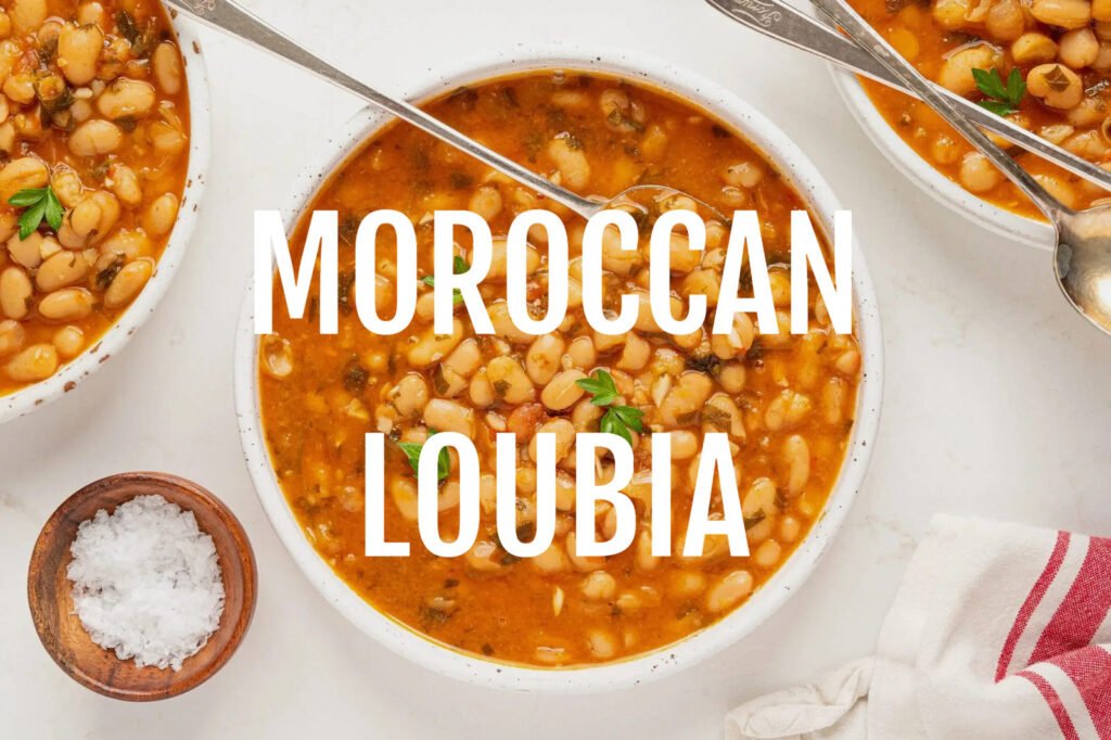 Bowl of Moroccan Loubia topped with parsley, surrounded by spoons, salt in a wooden bowl, and a red-striped cloth. Text ‘Moroccan Loubia’ overlays.