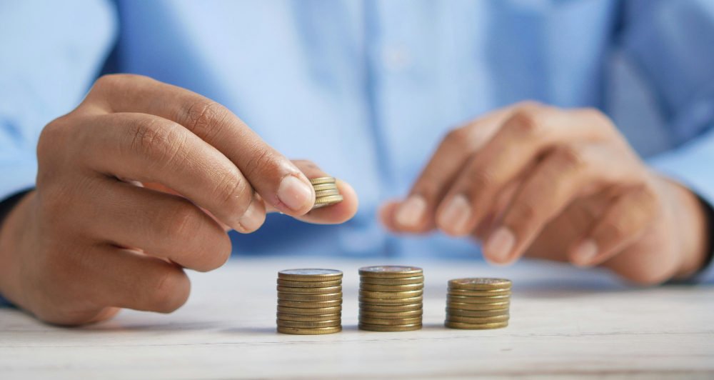 Hands stacking coins on a table, with three neat piles. Person wears a blue shirt. Scene suggests focus and precision.