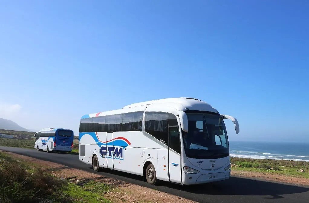 Deux cars CTM blancs et bleus roulant sur une route côtière au Maroc sous un ciel dégagé, l’océan en arrière-plan. Les cars CTM relient les villes du Maroc.