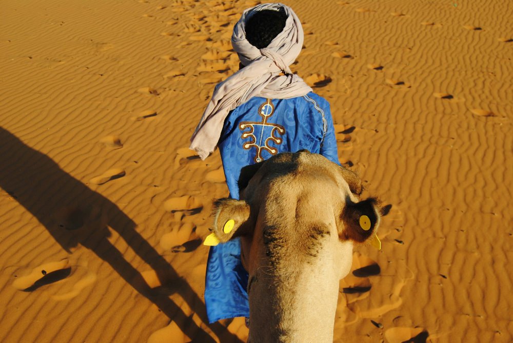 A local man wearing traditional clothes with his camel in the sahara in Morocco